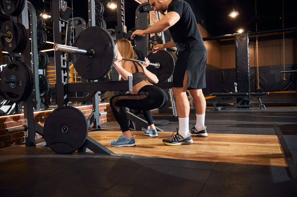 Professional fitness coach helping woman with weight-lifting